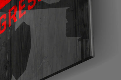 Close-up angled view of dark textured glass wall art with red printed text visible in upper left corner.