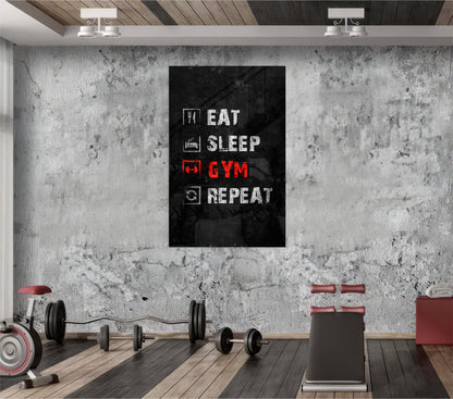 Black glass wall art displaying "Eat Sleep Gym Repeat" in white and red neon-style text, mounted in an industrial gym setting with concrete walls and exercise equipment.