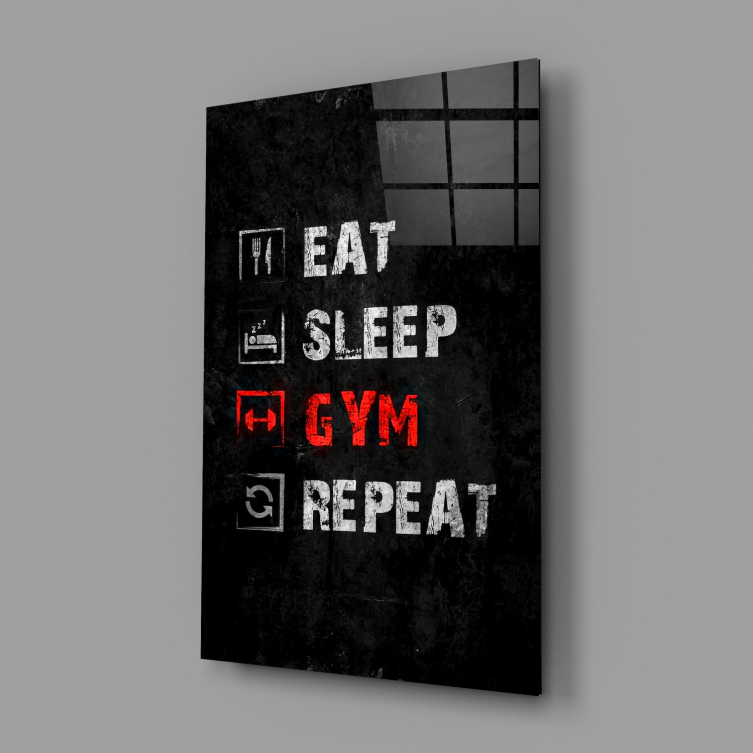 Black glass wall art panel displaying white text "EAT SLEEP" and red text "GYM REPEAT" with icons, shown at an angle against gray background.