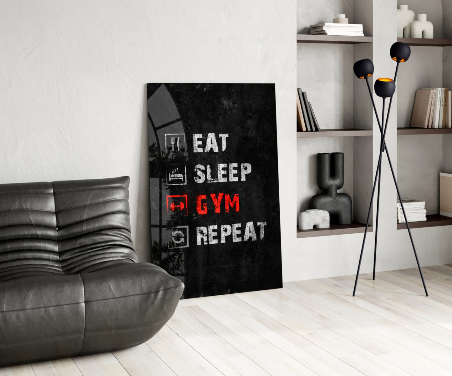 Black glass wall art with white and red text reading "Eat Sleep Gym Repeat" displayed in modern living room with gray sofa and shelving.