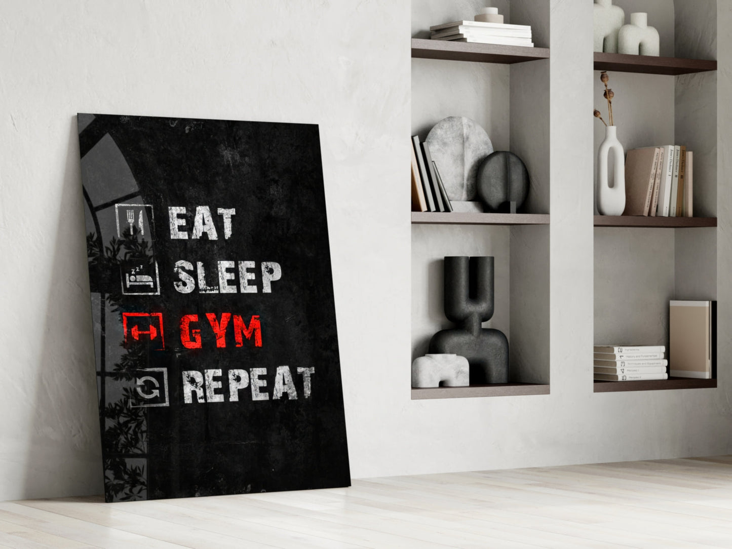 Black glass wall art with white and red "Eat Sleep Gym Repeat" text leaning against white wall next to wooden shelving.