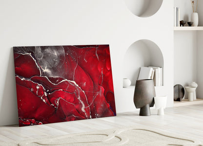 Red and grey marbled glass wall art leaning against white wall in minimalist interior display with decorative objects.