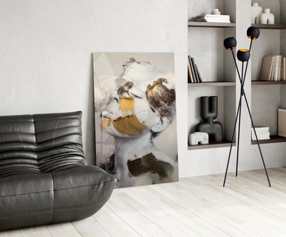 Modern living room featuring glass wall art depicting a woman's face with gold and charcoal brushstrokes, positioned between a black leather sofa and white shelving unit.
