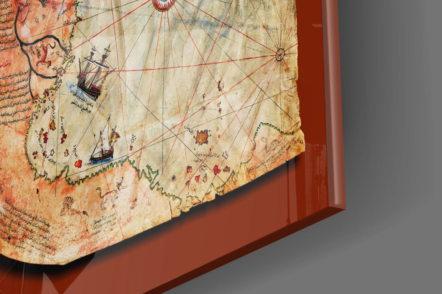 Angled view of Piri Reis map glass wall art showing aged parchment with red compass lines, ships, and Arabic text on burgundy frame.