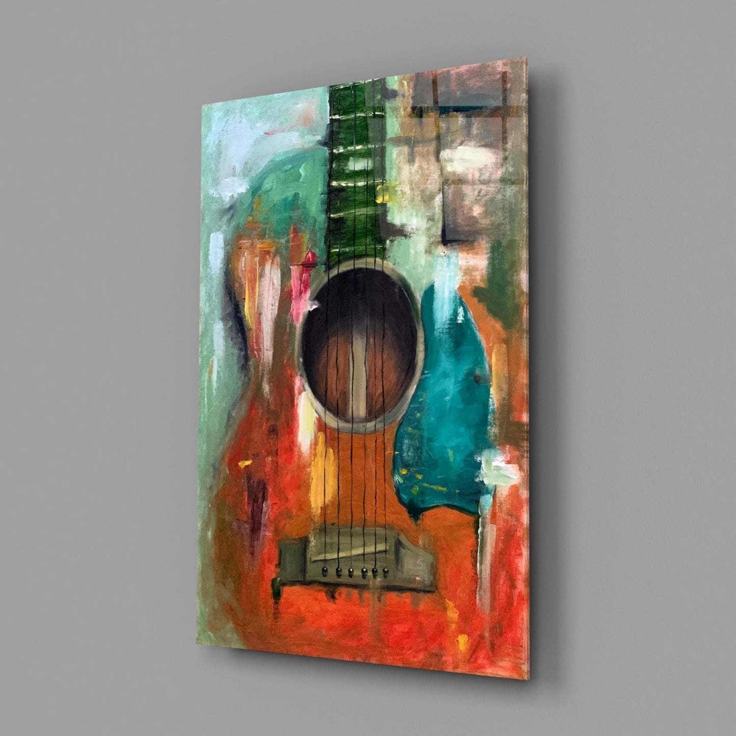 Angled view of a glass wall art piece featuring an acoustic guitar with colorful abstract paint effects in red, green, teal, and orange tones.
