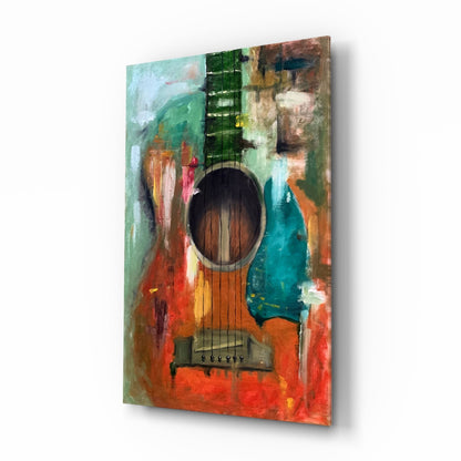 Colorful abstract guitar glass wall art displayed at an angle, showing vibrant red, orange, teal, and green painted background with black strings and sound hole detail.