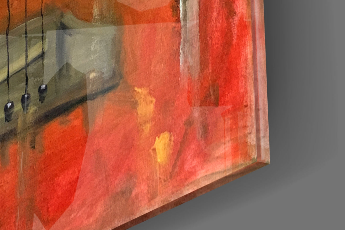 Close-up angled view of glass wall art showing red and orange watercolor gradients with hanging wire details and neutral gray background.