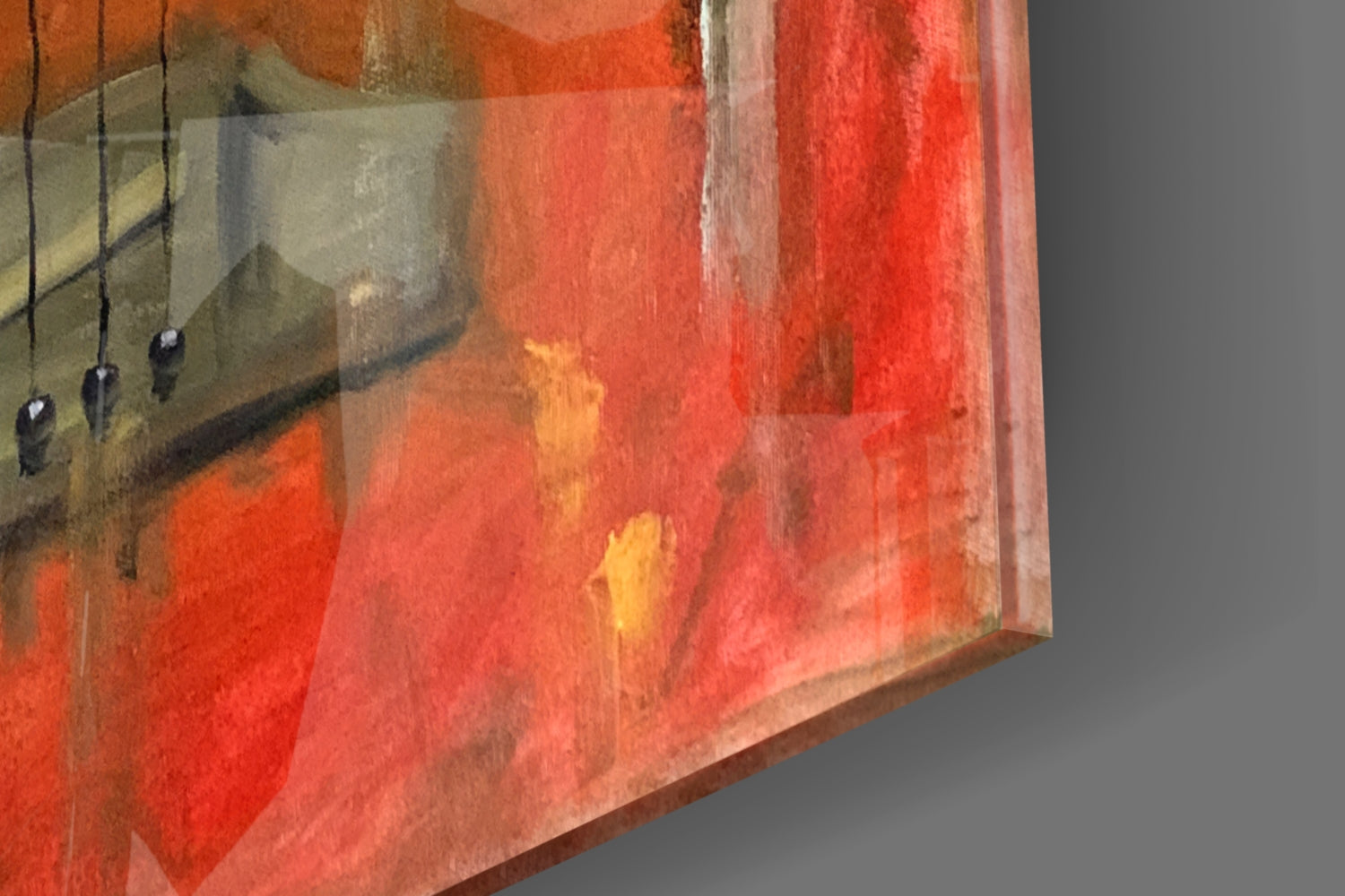 Close-up angled view of glass wall art showing red and orange watercolor gradients with hanging wire details and neutral gray background.