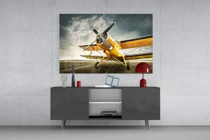 Yellow vintage aircraft displayed on glass wall art mounted above a dark gray media console in a modern interior setting.