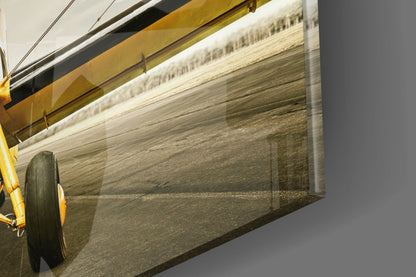 Close-up angled view of glass wall art displaying aerial farmland photograph with yellow mounting frame and black hardware visible.