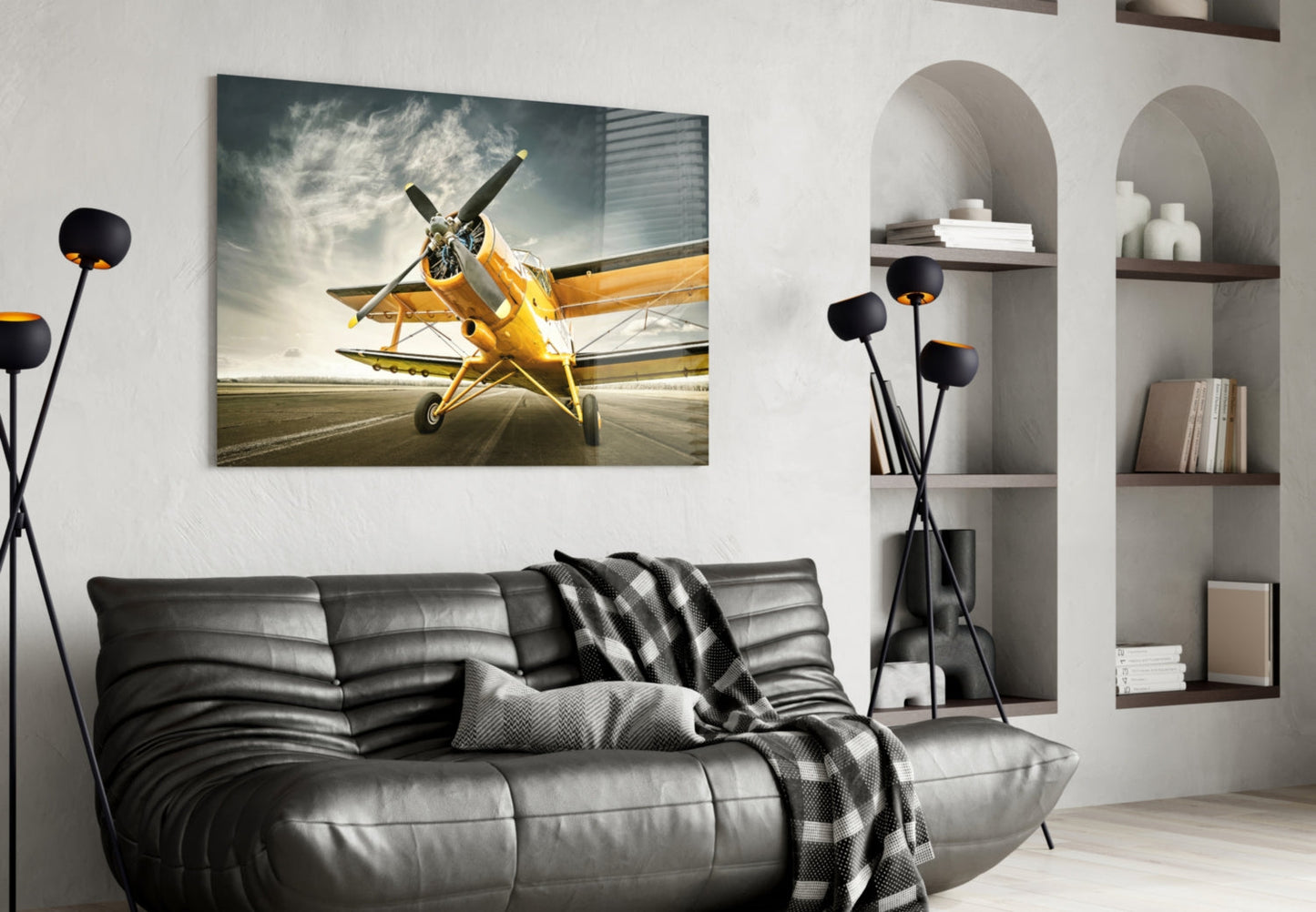 Yellow vintage aircraft on runway displayed as framed glass wall art above black leather sofa in modern living room.