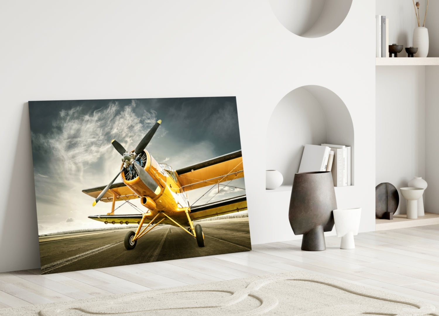 Yellow vintage biplane on runway displayed as glass wall art in minimalist interior setting with white shelving and decorative objects.