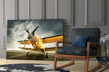 Yellow vintage biplane on runway displayed as glass wall art in modern living room with wooden chair.