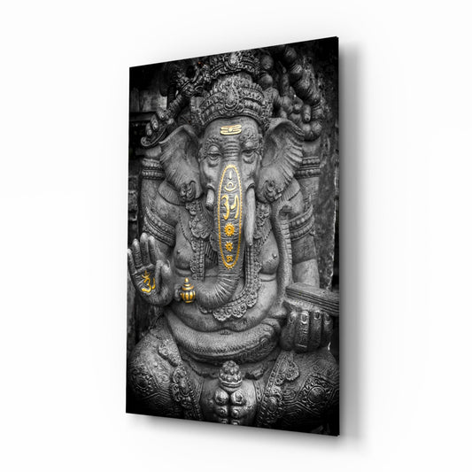 Stone statue of Ganesha with gold-accented details on trunk and forehead, displayed as a mounted glass wall panel.