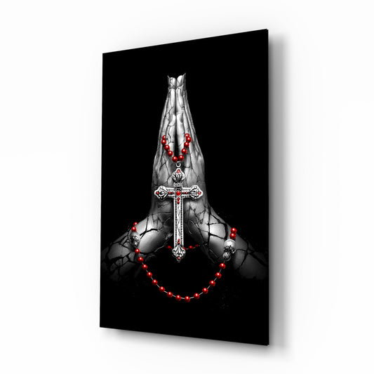 Angled view of glass wall art featuring praying hands with ornate cross and red glowing rosary beads on black background.