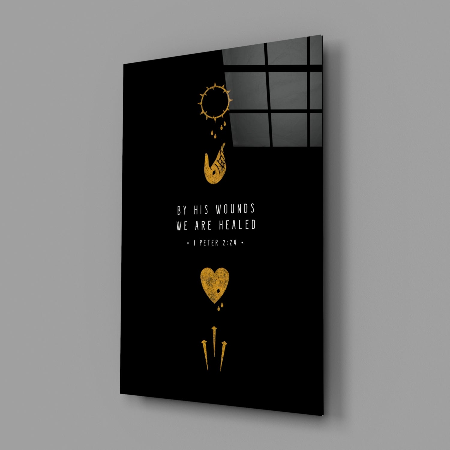 Black glass wall art panel with gold religious symbols and white text reading "BY HIS WOUNDS WE ARE HEALED - I PETER 2:24," displayed at an angle with window reflection visible.