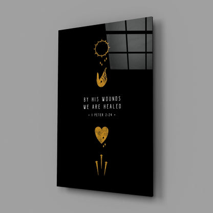 Black glass wall art panel with gold religious symbols and white text reading "BY HIS WOUNDS WE ARE HEALED - I PETER 2:24," displayed at an angle with window reflection visible.
