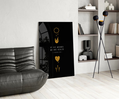 Black glass wall art with gold symbols and "By His Wounds We Are Healed" text displayed in modern living room setting.