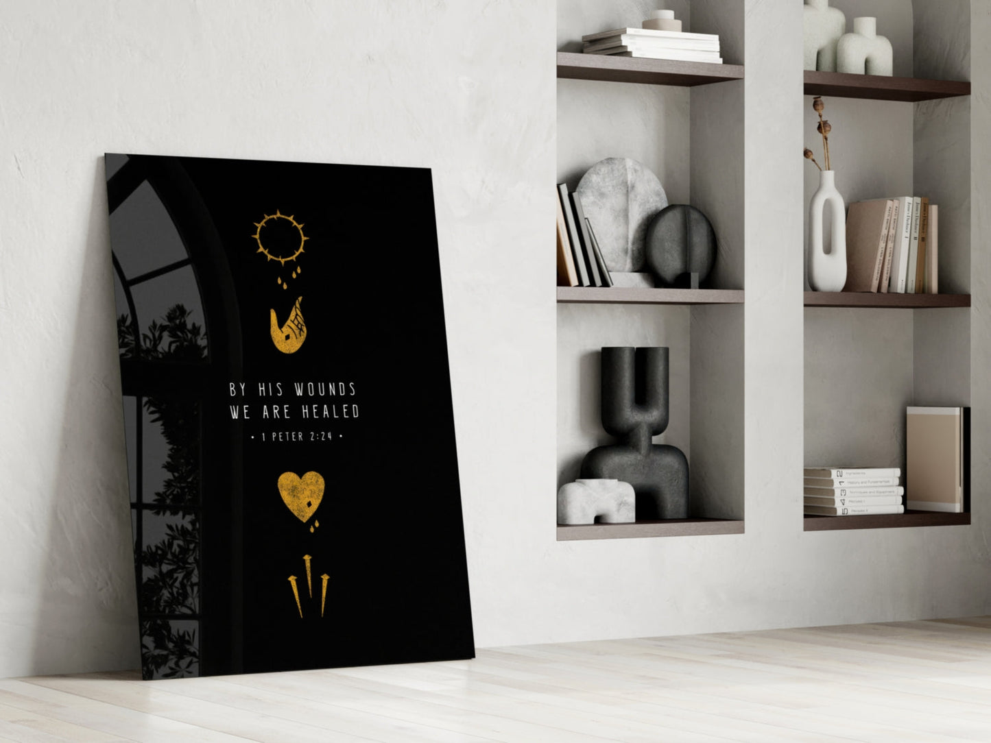Black glass wall art leaning against white wall displaying gold sun, hand, heart, and sword symbols with "By His Wounds We Are Healed" text, styled home setting with built-in shelving.