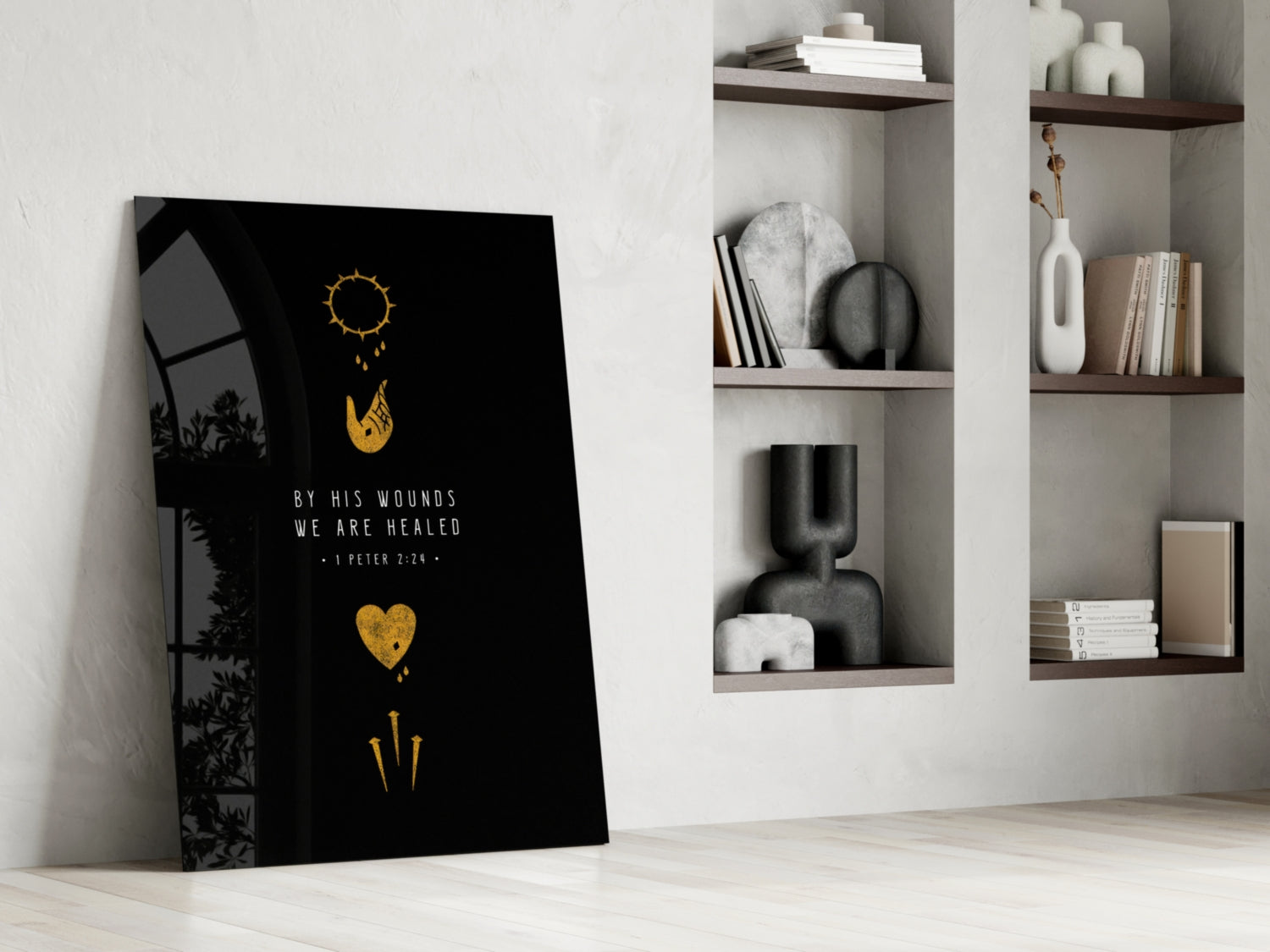 Black glass wall art leaning against white wall displaying gold sun, hand, heart, and sword symbols with "By His Wounds We Are Healed" text, styled home setting with built-in shelving.