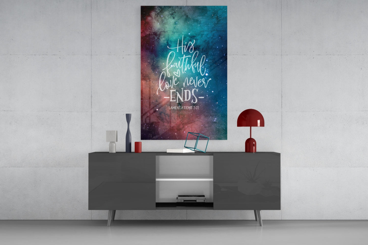 Galaxy-themed glass wall art with "His faithful love never ends" quote in white script displayed above gray media console.