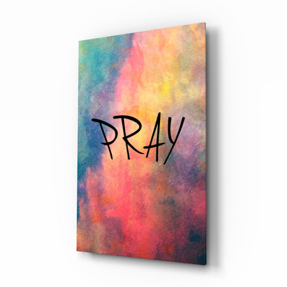 Angled view of glass wall art featuring "PRAY" text on vibrant watercolor gradient background with blues, pinks, yellows, and reds.
