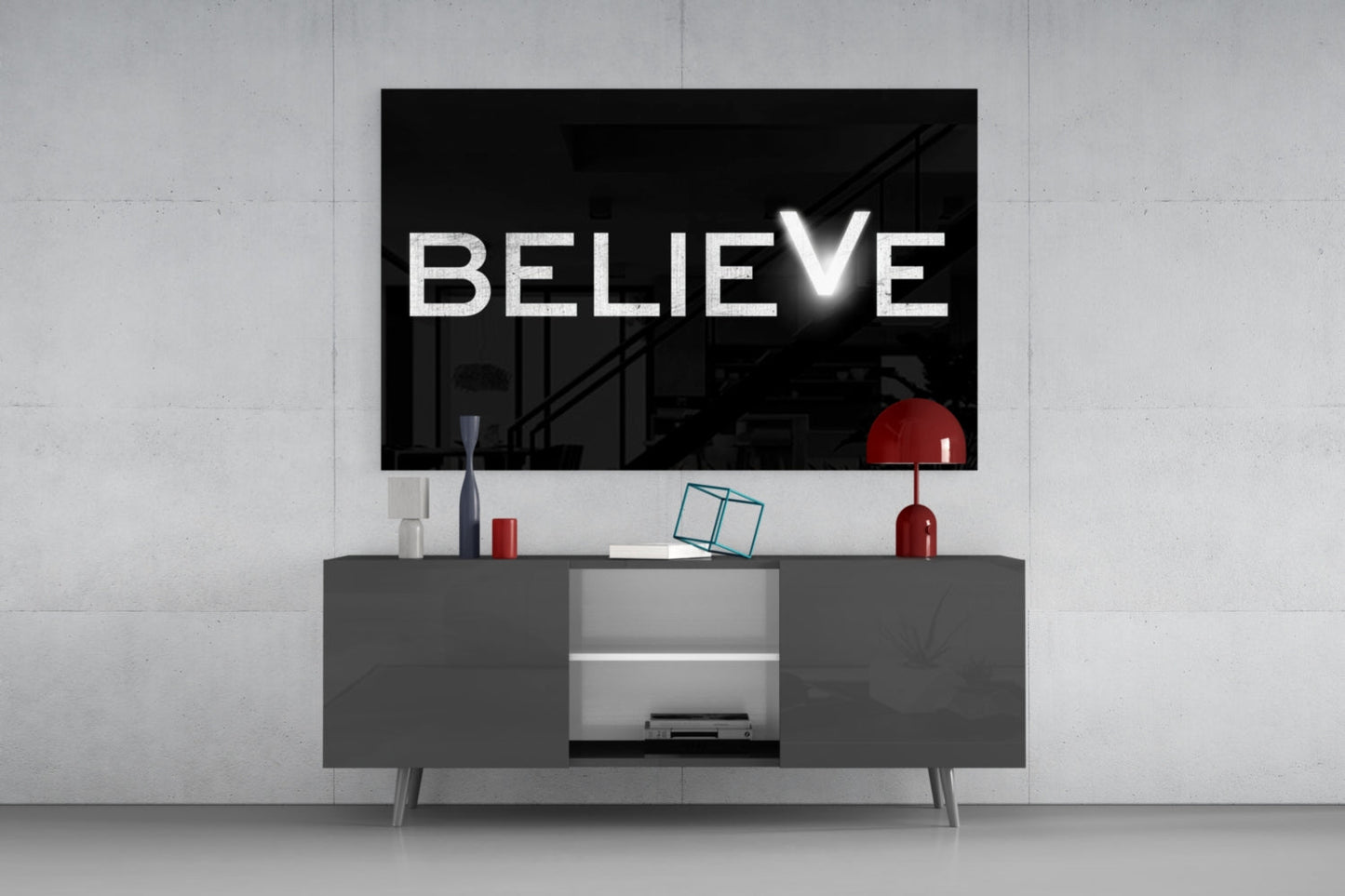 White "BELIEVE" text with checkmark on black glass mounted above gray media console with red decorative objects.