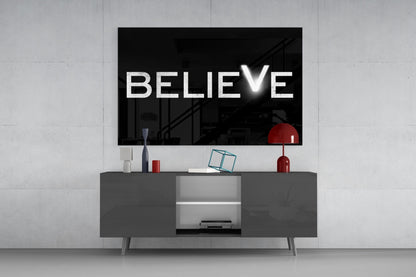 White "BELIEVE" text with checkmark on black glass mounted above gray media console with red decorative objects.