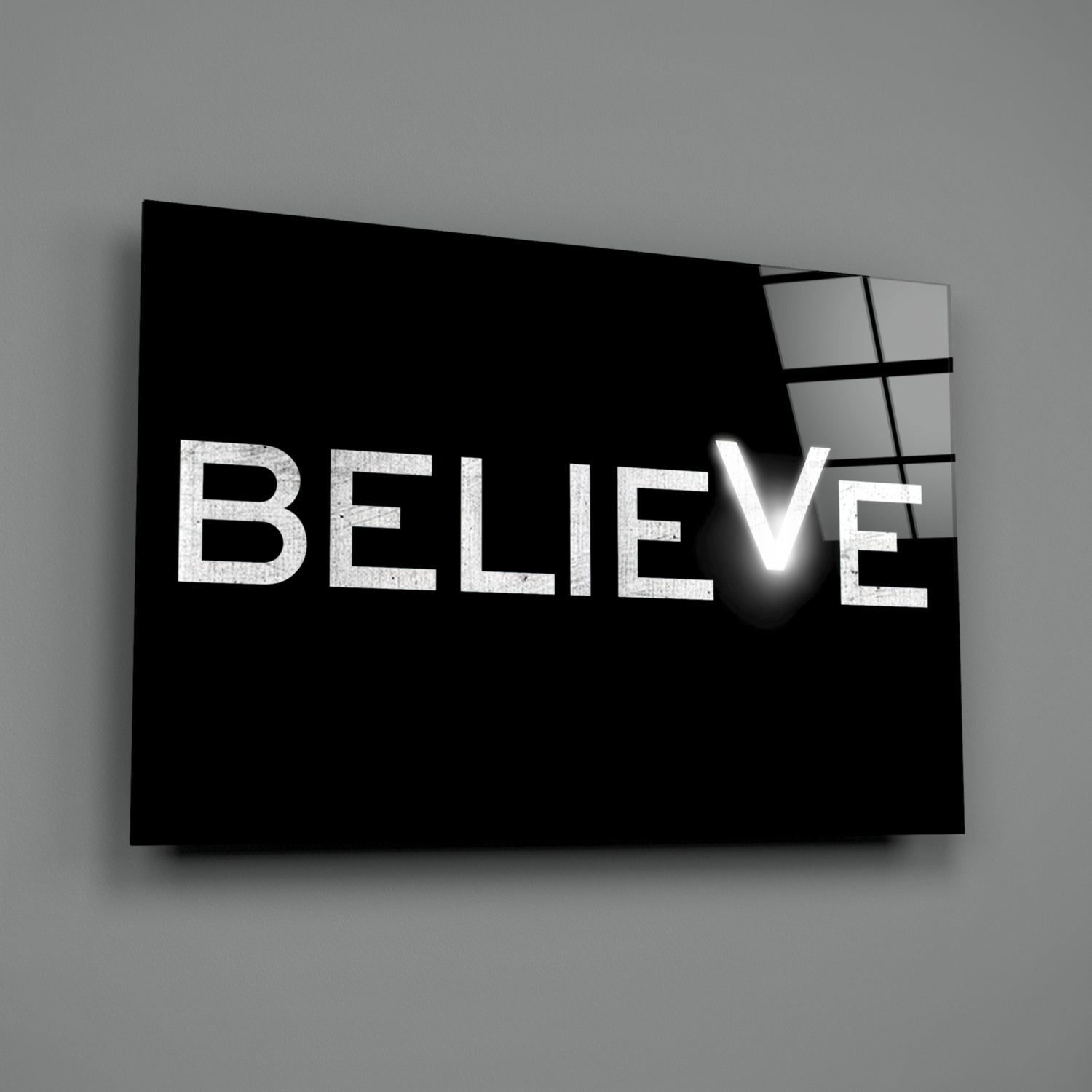 Black glass wall art panel with white "BELIEVE" text and illuminated checkmark, displayed at angle against gray background.