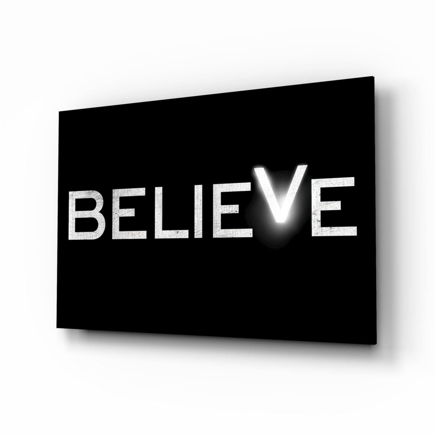 Black glass panel with white illuminated text spelling "BELIEVE" displayed at an angle with shadow effect.