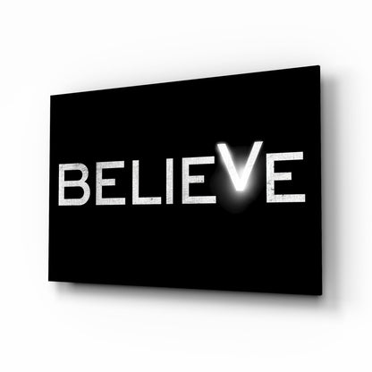 Black glass panel with white illuminated text spelling "BELIEVE" displayed at an angle with shadow effect.