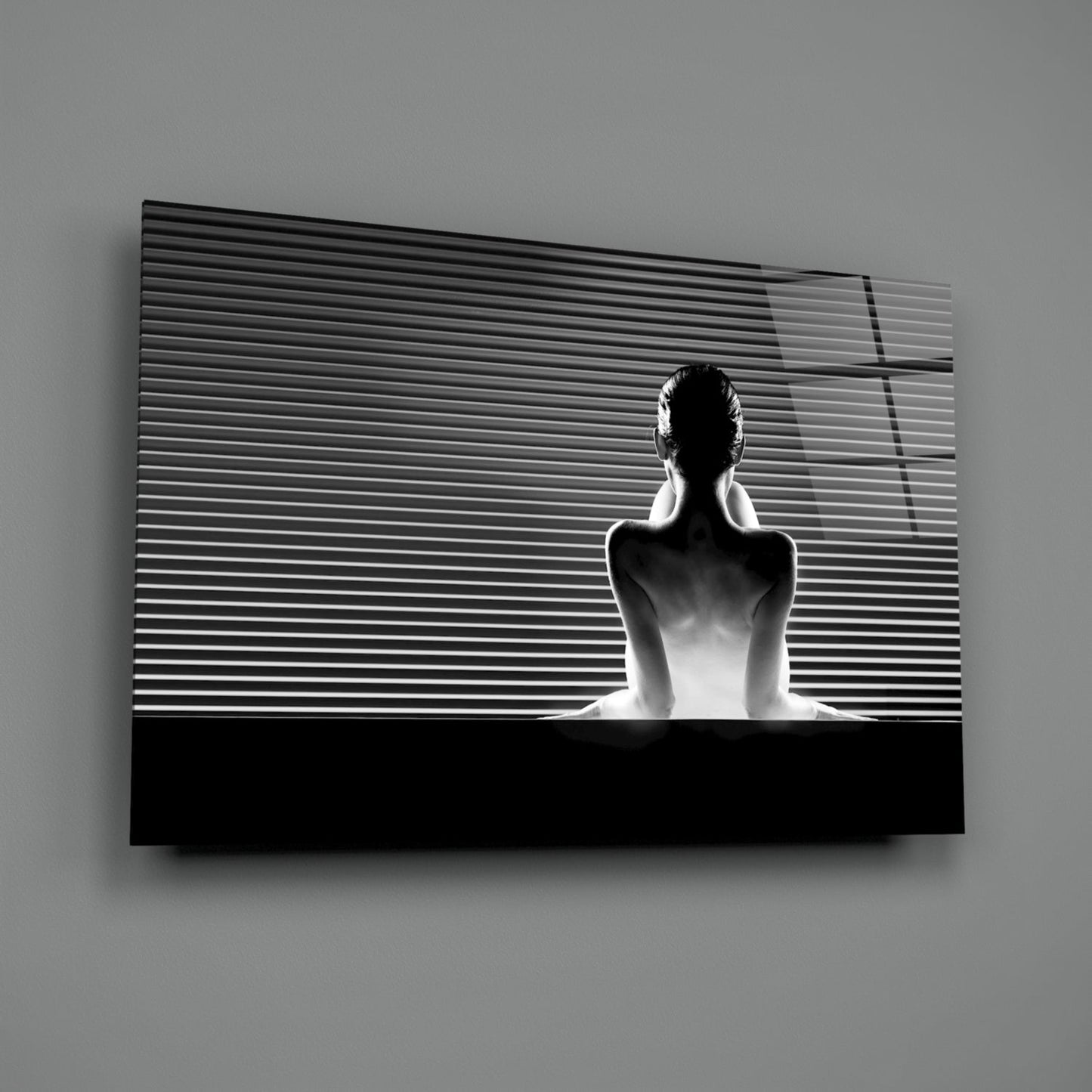 Black and white glass wall art depicting a bare-shouldered figure seated against horizontal linear patterns, mounted on gray wall.