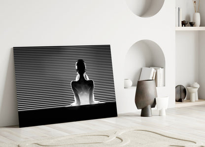 Black and white glass wall art featuring a silhouetted figure against horizontal lines, leaning against white wall in minimalist interior.