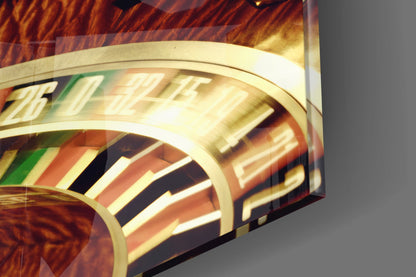 Close-up angled view of glass wall art with cream band, striped pattern in green, orange, black and white, and embossed text detail against warm wood-grain background.