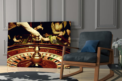 Gamble Glass Wall Art displaying a roulette wheel and casino scene with gold accents, mounted in a modern living room beside a wooden chair.