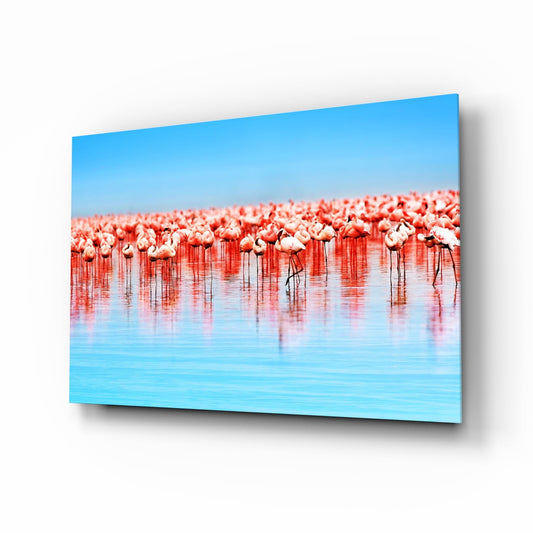 Angled view of glass wall art depicting a large flock of pink flamingos wading in shallow blue water under clear sky.