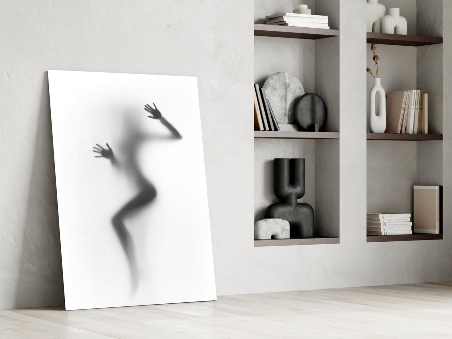 White canvas leaning against wall displays silhouetted female figure with raised arms beside wooden shelving with books and decorative objects.
