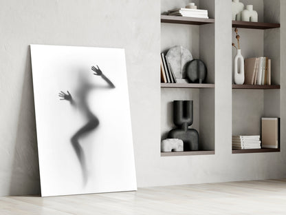White canvas leaning against wall displays silhouetted female figure with raised arms beside wooden shelving with books and decorative objects.
