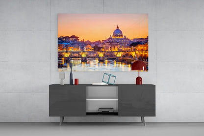 St. Peter's Basilica glass wall art displaying illuminated Rome cityscape with golden dome and bridge at twilight, mounted above gray media console.