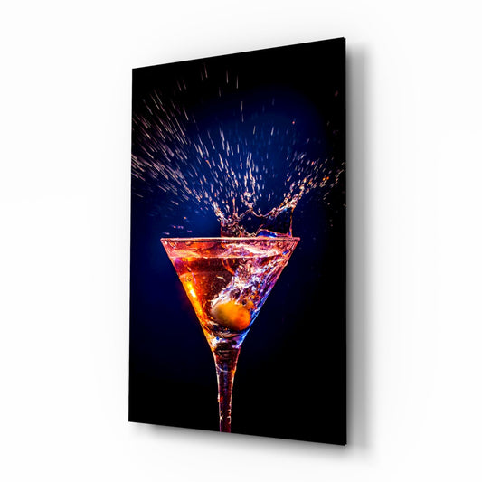 Angled three-quarter view of glass wall art featuring a martini glass with amber liquid and an olive, splashing upward against a dark blue background.