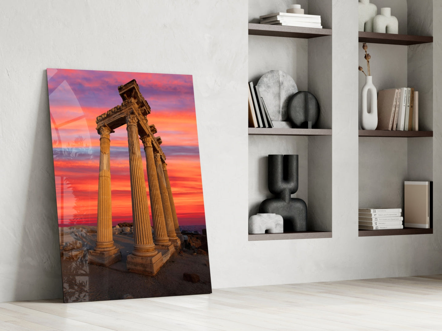Temple of Apollo glass wall art leaning against white wall beside shelving unit, showing ancient columns at sunset.