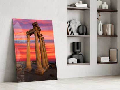 Temple of Apollo glass wall art leaning against white wall beside shelving unit, showing ancient columns at sunset.