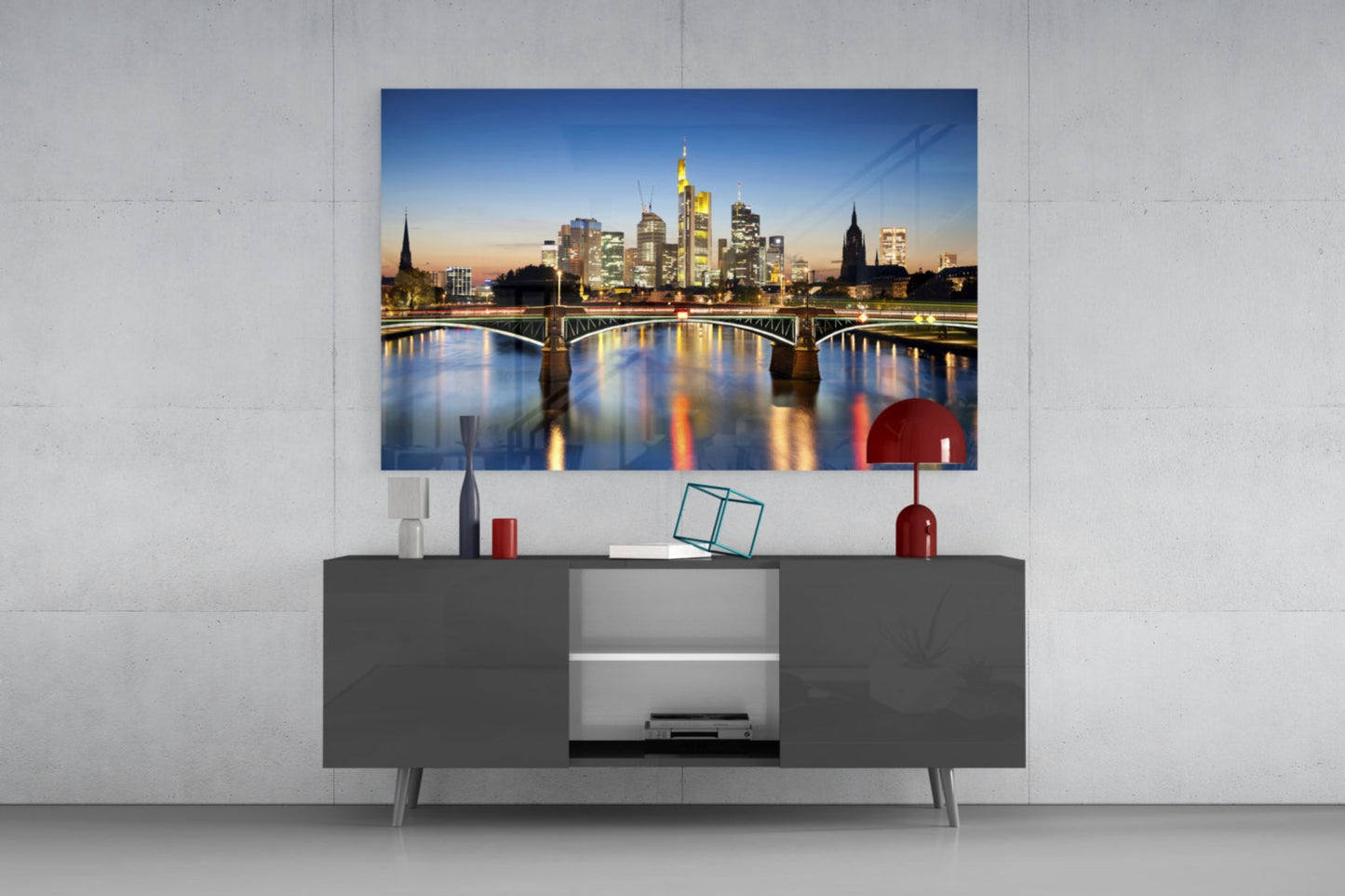 Frankfurt skyline glass wall art displayed above a dark gray media console with red decorative accessories in a modern living room.