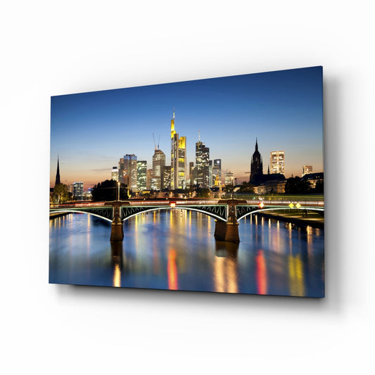 Frankfurt skyline at dusk reflected in Main River with illuminated bridge and buildings on glass panel.