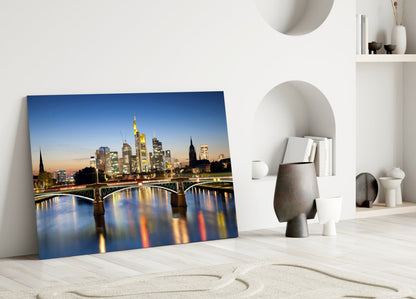 Frankfurt cityscape glass wall art leaning against white wall in minimalist interior setting.