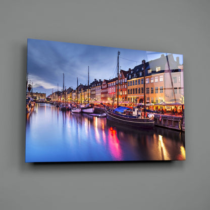 Nyhavn glass wall art mounted on gray wall displaying illuminated harbor scene with colorful buildings, boats, and water reflections at twilight.