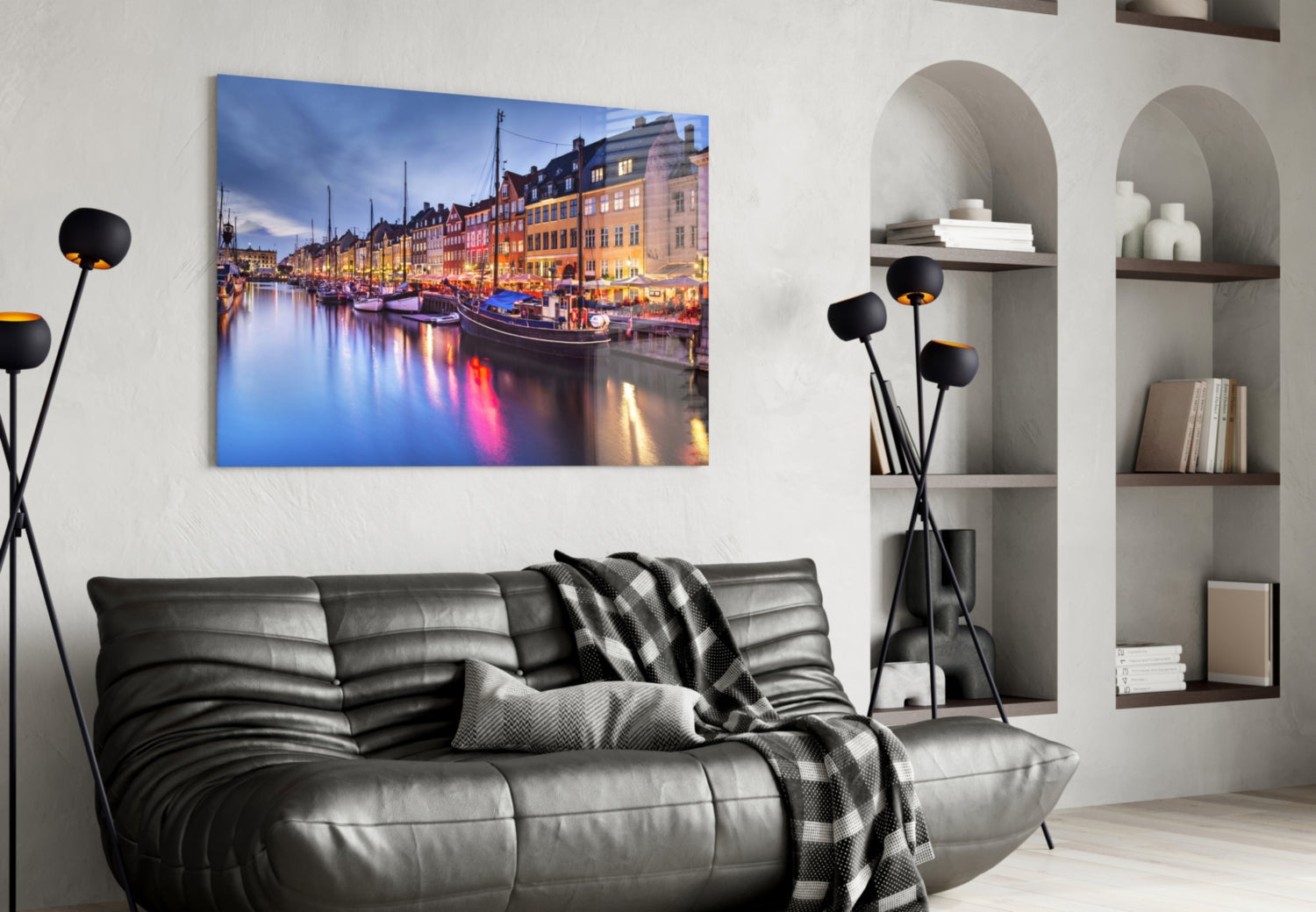 Nyhavn glass wall art displaying illuminated colorful buildings and boats reflecting in water, hung above black leather sofa in modern living room.