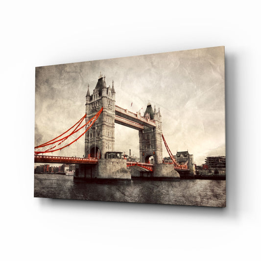 Tower Bridge Glass Wall Art displayed at an angle showing the vintage-style photograph with red bridge cables and stone towers over grey water.