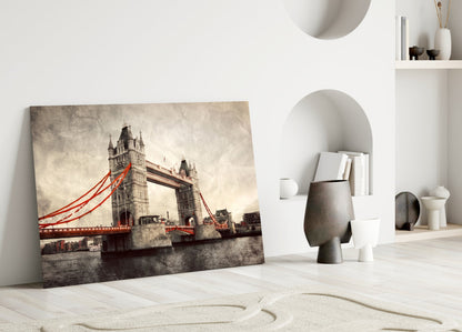 Tower Bridge glass wall art leaning against white wall in minimalist room setting, showing sepia-toned bridge with red cables.