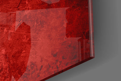 Red translucent glass wall art panel with textured surface and architectural imagery, photographed at angle against gray background.